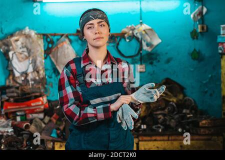 Portrait d'une jeune femme mécanicien en uniforme, portant des gants. Salle de travail en arrière-plan. Banque D'Images