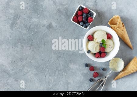 La crème glacée à la vanille ramasse avec de la framboise et du bleuet dans un bol vue du dessus sur fond gris. Dessert d'été rafraîchissant. Banque D'Images