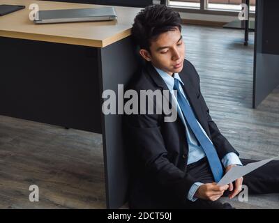 Un jeune homme d'affaires asiatique recevant de mauvaises nouvelles avec une lettre de licenciement, fatigué, stressé et triste assis avec l'esprit absent sur le terrain au pouvoir. Freustrat Banque D'Images