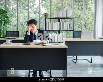 Un jeune homme d'affaires asiatique recevant de mauvaises nouvelles avec une lettre de licenciement, fatigué, stressé et triste assis avec l'esprit absent sur son bureau en fonction. Frustré Banque D'Images