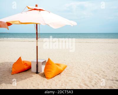 Parasols de plage orange et chaises de sac de haricots sur la plage de sable sur fond bleu ciel avec espace de copie, style minimal. Banque D'Images
