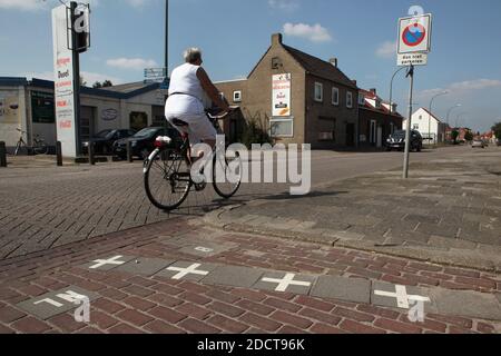 Le cycliste traverse la frontière compliquée entre la Belgique et les pays-Bas dans la ville de Baarle-Nassau aux pays-Bas. Le petit exclave hollandais d'où la photo a été prise est entouré par l'enclave belge ici. La maison en brique de l'autre côté de la rue en arrière-plan est située sur le territoire hollandais et appartient à une autre exclave hollandaise. La partie belge de la ville est connue sous le nom de Baarle-Hertog. Banque D'Images