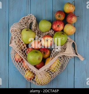 Couche plate de pommes biologiques dans un sac en filet écologique sur un plateau rustique bleu. Vegan, zéro plastique, concept écologique Banque D'Images