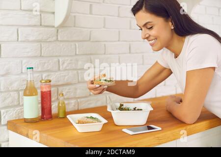 Bonne jeune femme appréciant une salade de légumes à emporter et un sandwich sains à la maison Banque D'Images