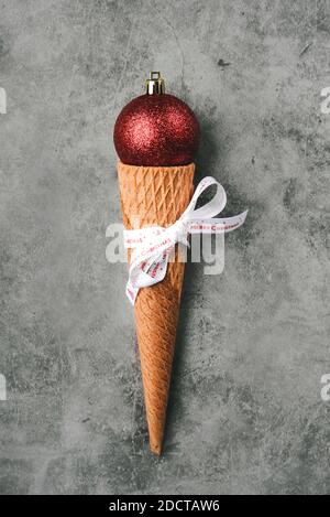 Arrière-plan du concept de Noël. Boule rouge de Noël en cône de crème glacée sur fond gris Banque D'Images