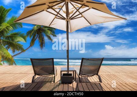 Plage ensoleillée avec parasol et chaises longues sur parquet, palmiers et mer turquoise sur Paradise Island. Banque D'Images