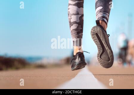 Femme mince qui court sur la route. Les pieds de la course à pied sur la route près de la chaussure Banque D'Images