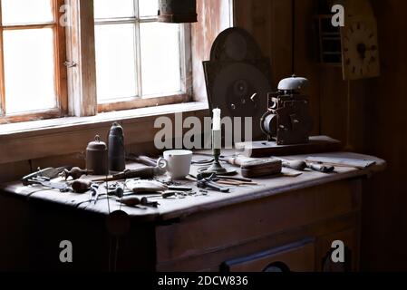 Atelier des horlogers avec des outils et des pièces d'horloge parsemées sur la table avec la lumière naturelle en streaming à travers la fenêtre. Banque D'Images