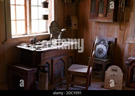 Atelier des horlogers avec des outils et des pièces d'horloge parsemées sur la table avec la lumière naturelle en streaming à travers la fenêtre. Banque D'Images