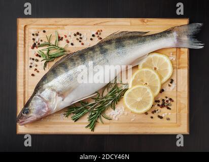 Brochet frais non cuit avec citron, romarin et épices sur panneau de bois sur fond noir Banque D'Images