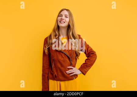 belle fille heureuse attrayante, dans une robe jaune vif et veste d'automne, pose sur un fond jaune isolé. Le concept de l'automne Banque D'Images