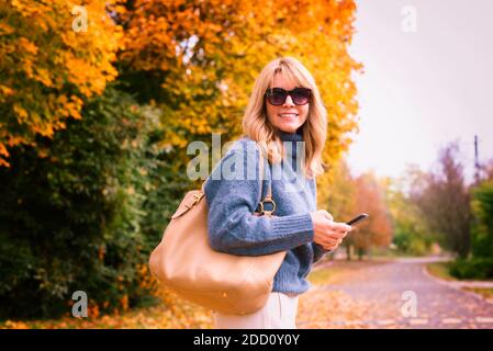 Portrait de la femme d'âge moyen avec messagerie texte tout en marchant dans la rue en automne. Banque D'Images