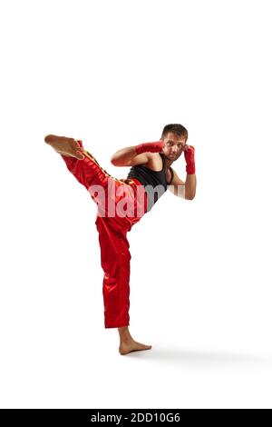 Homme sportif dans les bandages de sport rouges sur ses mains faisant le coup de pied pendant l'exercice de boxe, isolé sur fond blanc. Longueur complète Banque D'Images