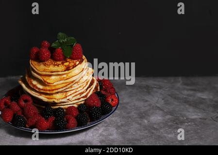 Une pile de crêpes maison sur une assiette avec framboises et mûres sur fond sombre . Le concept de pâtisseries maison. Banque D'Images