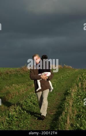 Père transportant une fille de quatre ans loin de la tempête. Octobre. Rundle Hill, South Downs, Goodwood, près de Chichester, West Sussex, Angleterre Banque D'Images