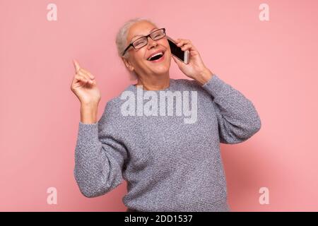 Bonne joyeuse femme en train de parler à un ami sur un téléphone mobile, en riant. Studio tourné sur un mur rose Banque D'Images