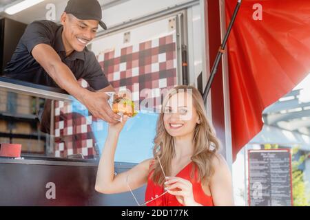 Belle femme qui a un hamburger comme plats à emporter de la cuisine dans un camion alimentaire Banque D'Images