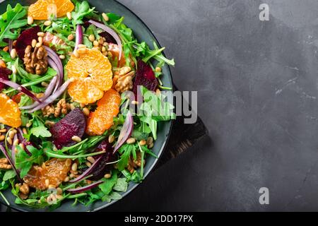 Salade de mandarine et de betteraves maison avec roquette, noix et pignons sur fond de béton gris. Nourriture végétalienne saine. Vue de dessus. Gros plan. Espace Banque D'Images