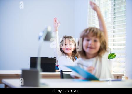 De jolis petits élèves levant les mains pendant la leçon. Enfants en classe à l'école. Banque D'Images