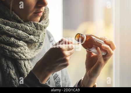 femme malade avec foulard autour du cou prenant du sirop contre la toux à la maison Banque D'Images