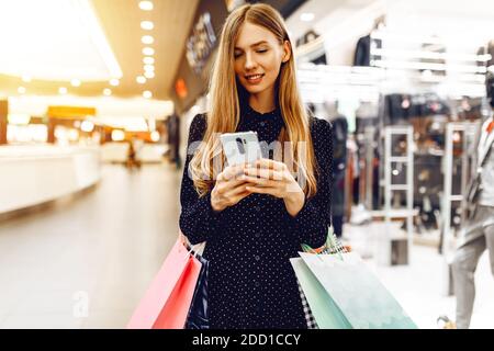 belle jeune femme dans une robe, avec des sacs de shopping, utilise un téléphone mobile dans un centre commercial Banque D'Images