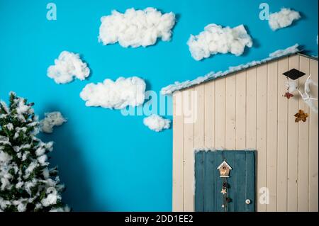 Studio décoratif de Noël avec une maison avec porte bleue, banc en bois et skis, bonhomme de neige, faux nuages et neige Banque D'Images