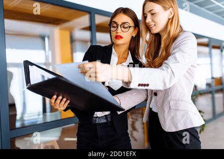 De jeunes collègues d'affaires heureux communiquent tout en marchant le long du couloir dans le bureau avec un dossier avec des documents Banque D'Images