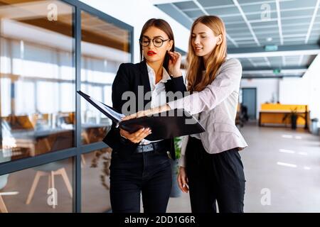 De jeunes collègues d'affaires heureux communiquent tout en marchant le long du couloir dans le bureau avec un dossier avec des documents Banque D'Images