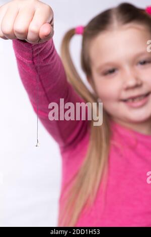 Une petite fille en rose tient une dent de lait arrachée sur un filetage Banque D'Images