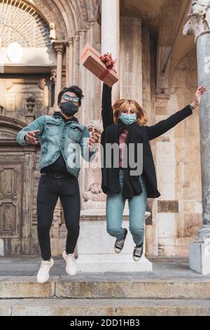 jeune couple heureux portant un masque au moment du saut du coronavirus avec un cadeau en main Banque D'Images