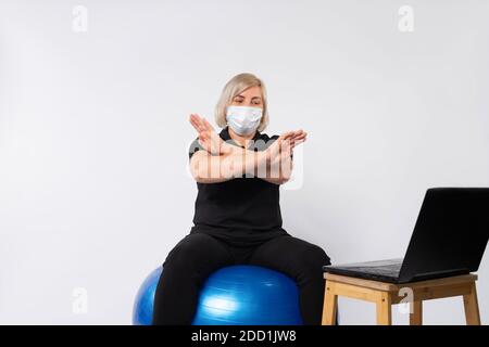 Femme âgée, fitness à la maison, masque médical montre virus d'arrêt. Arrière-plan blanc. Banque D'Images