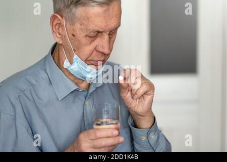 Un homme âgé dans un masque médical prend une pilule. Problèmes de santé à la vieillesse, processus de vieillissement. Banque D'Images