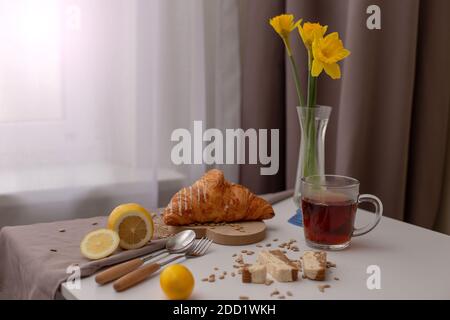 Le petit-déjeuner comprend une tasse de thé, des croissants, des citrons et du narcis jaune dans un vase en verre Banque D'Images