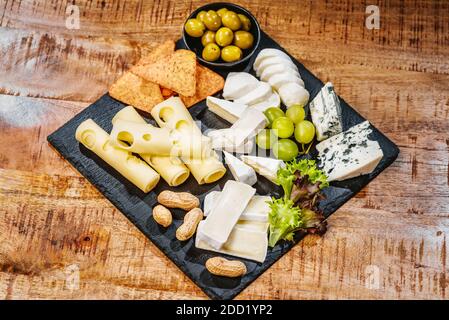 Assiette de fromages, un ensemble de fromages différents sur une assiette noire avec des raisins et des olives vertes et des noix.gros plan Banque D'Images