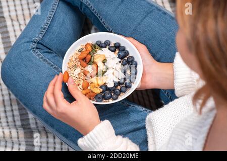 Granola fraîche, muesli avec yaourt, fruits et baies dans les mains des filles. Gros plan.fille avec une assiette de flocons d'avoine avec des noix et des mûres. Une alimentation saine, Banque D'Images