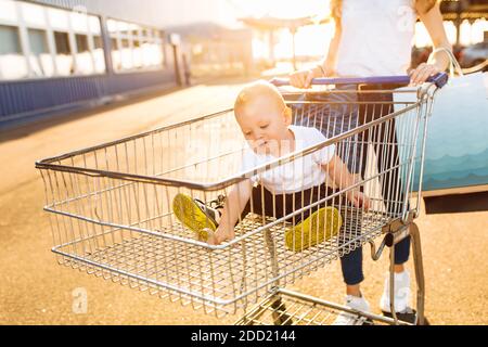 Bonne belle jeune mère et petit enfant dans un magasin marche en chariot avec des sacs de shopping dans la ville sur le arrière-plan d'un centre commercial Banque D'Images