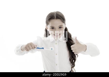 Brillant fille sourire parfait est titulaire brosse à dents avec goutte de pâte blanc arrière-plan. Brosse à dents enfant tient et montre Thumbs up. Enfant heureux d'écolière soins du visage hygiène buccale. Sourire brillant concept. Banque D'Images