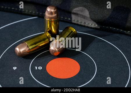 Munitions de pistolet en vrac dispersées sur une cible en papier avec un fond de camouflage. L'arrière-plan et le premier plan sont flous avec un dé peu profond Banque D'Images