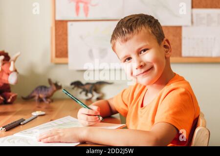 Adorable enfant garçon dessin dinosaures sur la photo avec des crayons de couleur assis près d'un bureau dans sa chambre Banque D'Images