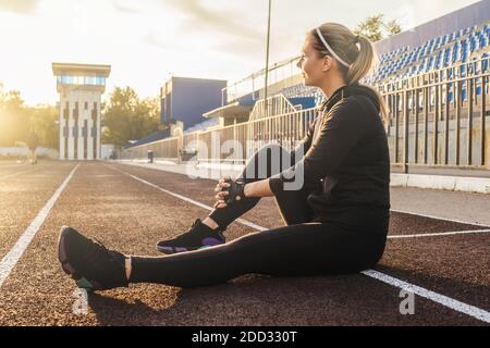 Forme physique sourire femme portrait style de vie en noir tracksuit extérieur, blanc ciel ensoleillé fond. Lumière de coucher de soleil, mise au point sélective. Banque D'Images