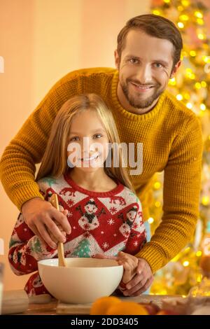 Fille et son père remuant quelque chose dans un bol et sourire Banque D'Images