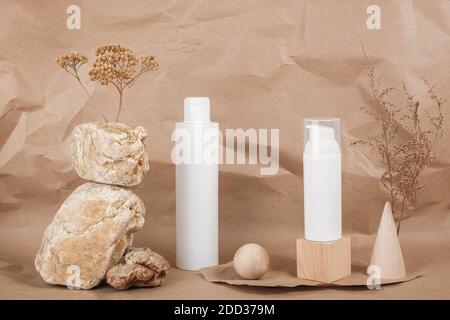 Deux bouteilles de cosmétiques blanches avec crème, sérum ou autre produit cosmétique, pierres, forme géométrique, fleurs séchées sur fond beige. Natura Banque D'Images