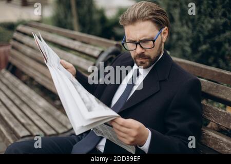 Homme assis sur le banc et reading newspaper Banque D'Images