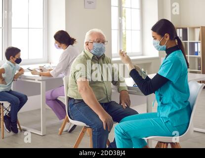 Patient âgé sous masque facial ayant reçu un vaccin contre la grippe, la pneumonie ou Covid-19 dans une clinique moderne Banque D'Images