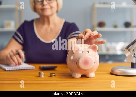 Femme âgée femme assise avec des notes et mettant des pièces à porcgybank pour économiser de l'argent Banque D'Images