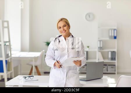 Femme médecin en uniforme médical blanc debout avec des documents et regarder l'appareil photo Banque D'Images