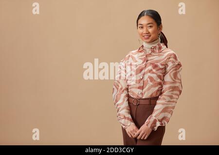 Portrait d'une femme asiatique belle en vêtements élégants posant contre l'arrière-plan beige Banque D'Images