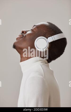 Vue latérale de l'homme africain dans un casque sans fil appréciant le musique isolée sur fond gris Banque D'Images