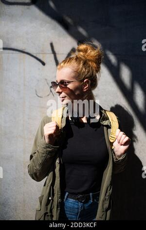 Portrait de la jeune femme heureuse avec des cheveux rouges dehors en ville, portant des lunettes de soleil. Banque D'Images