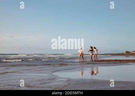 Groupe de trois jeunes femmes portant des maillots de bain ou des vêtements décontractés d'été, marchant pieds nus sur la plage, tout en parlant, en riant et en appréciant, El Medano Banque D'Images